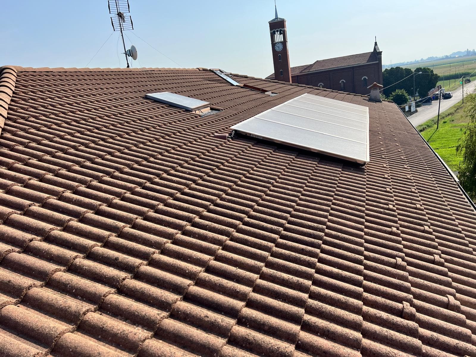 Copertura COESA prima dell'installazione fotovoltaica con solare termico esistente e chiesa sullo sfondo