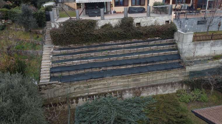 Realizzazione fotovoltaica iS ENERGY a San Pietro Val Lemina: Vista generale ante operam del terrazzamento inclinato davanti all abitazione, con filari esistenti e geometria a gradoni.